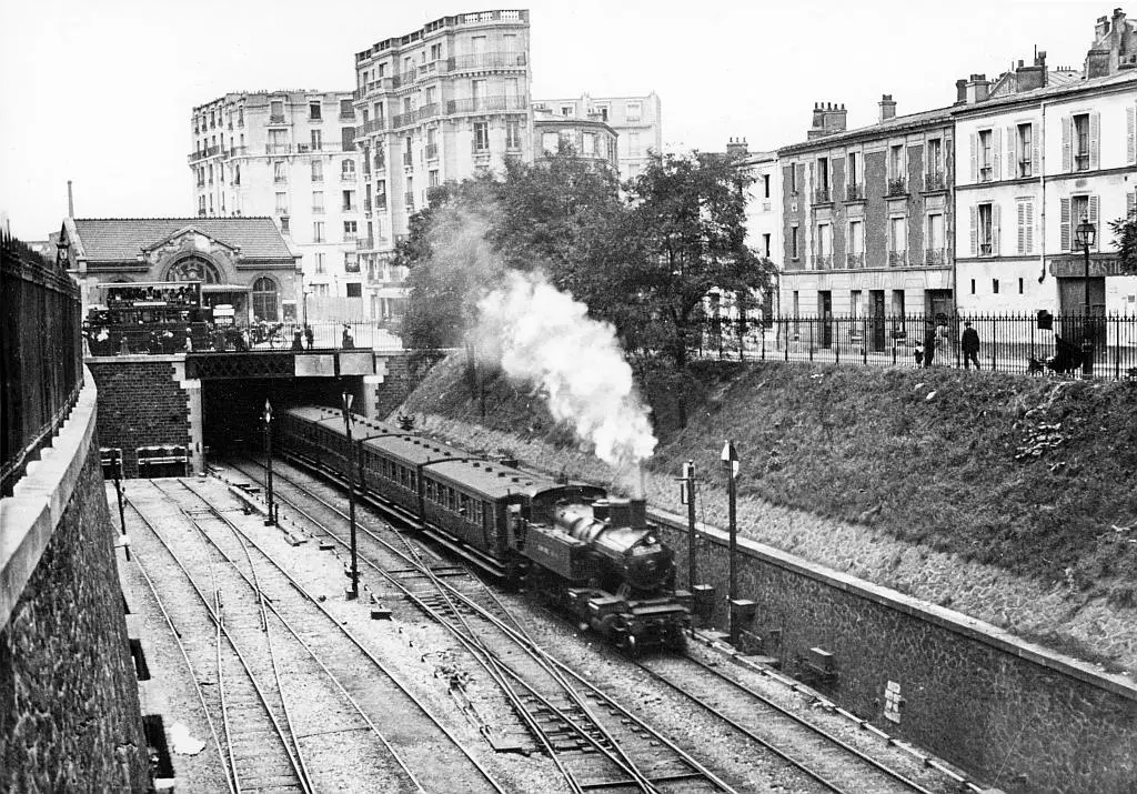 Un train en direction de Courcelles-Ceinture quitte la station de l'Avenue de Saint-Ouen en passant devant le raccordement des docks de Saint-Ouen